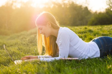 Bir dizüstü bilgisayar ile genç güzel kadın öğrenci çim, i yatıyor