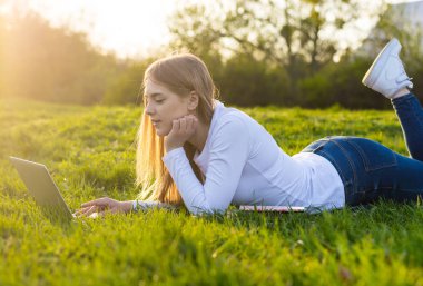 Genç güzel kadın öğrenci bir dizüstü bilgisayar ile çim üzerinde yalan