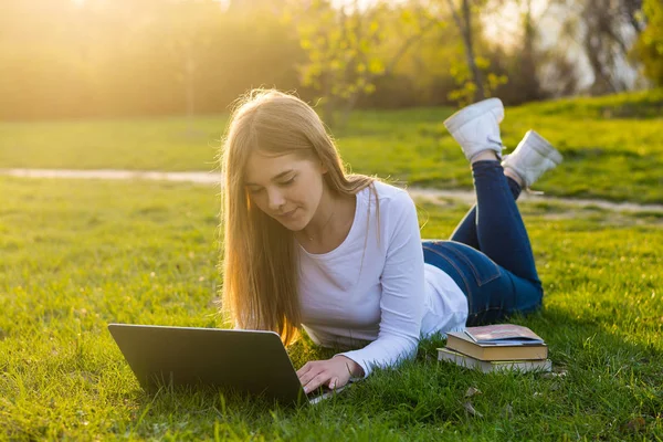 Joven hermosa mujer estudiante con un portátil se encuentra en la hierba en —  Fotos de Stock