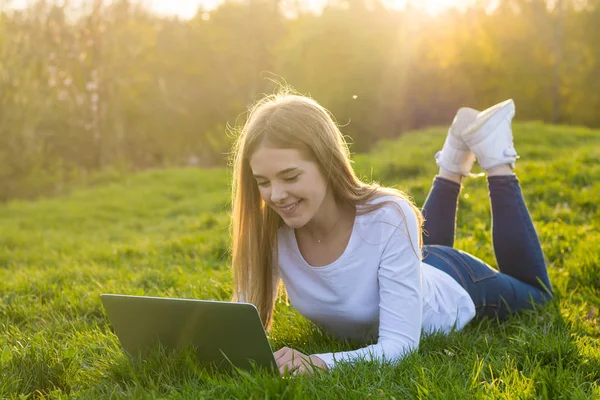 Joven hermosa estudiante con un ordenador portátil se encuentra en la hierba, i —  Fotos de Stock