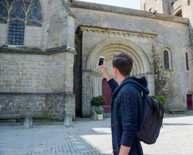Sırt çantalı genç bir adam Fransa 'nın ortaçağ şehri Carcassonne' daki La Basilique Saint-Nazaire 'de akıllı telefonla ateş ediyor.