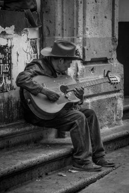Gitarlı bir adam sokakta oturuyor.