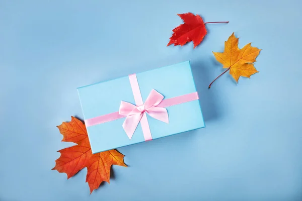 Niebieskie pudełko z atlas różowa wstążka na niebieskim tle z jasnym jesienią liście — Zdjęcie stockowe