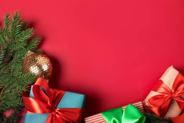 Katı kırmızı arka planda renkli atlas kurdeleleri olan üç parlak noel hediyesi.