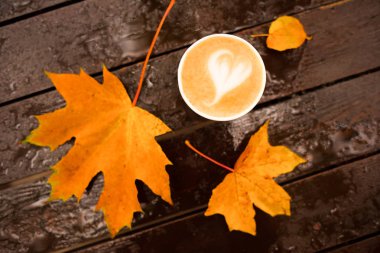 Dışarıdaki ıslak ahşap masada akçaağaç yapraklı kahve kağıdı fincanı.