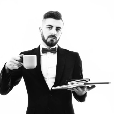 Takım elbiseli sakallı işadamı dizüstü bilgisayar, organizatör ve mavi kupa tutuyor.