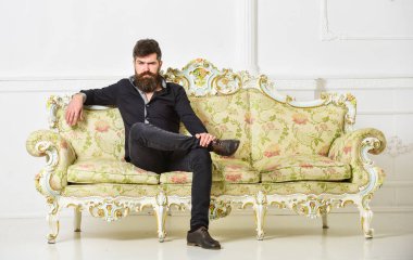 Hipster sıkı yüzünde yalnız oturuyor. Zengin ve yalnız kavramı. Lüks daire sahibi beyaz duvar arka koltukta oturur. Sakallı ve bıyıklı lüks oturma odasında boş zaman harcıyor