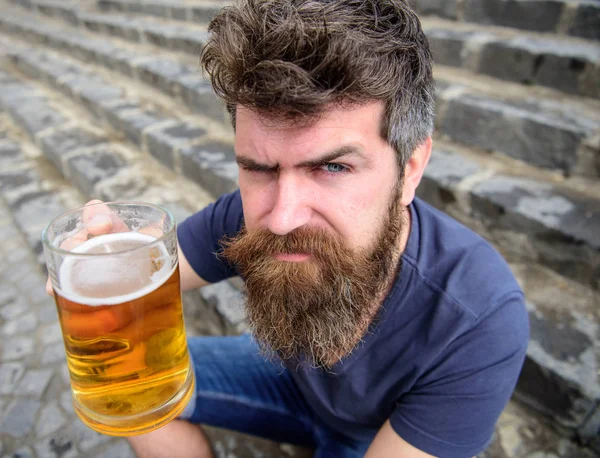 Hipster na ścisłe twarz picie piwa na zewnątrz, podniesienie napój. Koncepcja okrzyki. Człowiek z broda i wąsy posiada szkło z piwem, podczas gdy siedzi na kamienne schody. Facet po odpoczynku z zimne piwo — Zdjęcie stockowe