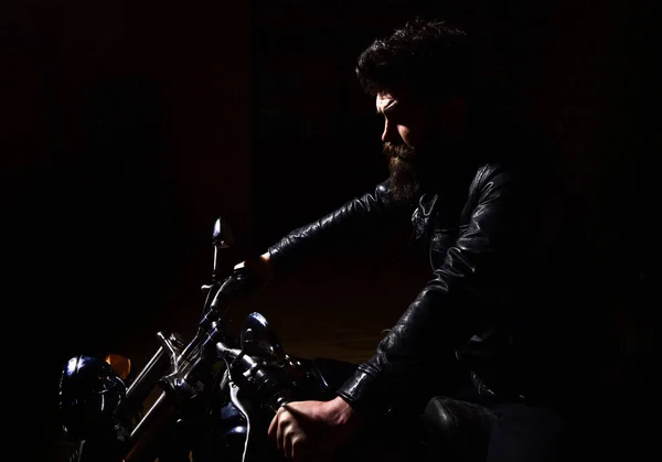 Manlighet koncept. Mannen med skägg, biker i skinnjacka sitter på motorcykel i mörker, svart bakgrund. Macho, brutal biker i läder jacka Rider motorcykel nattetid, kopia utrymme — Stockfoto