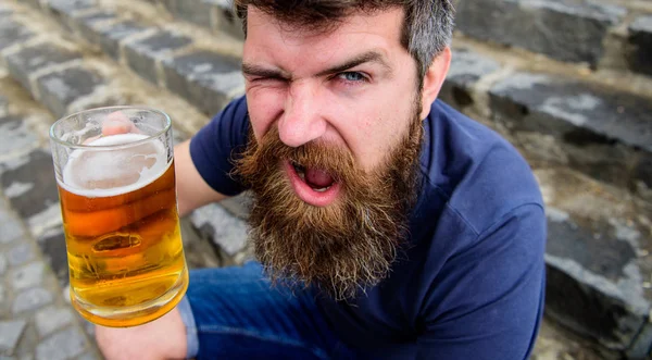Viering concept. Man met baard en snor houdt glas met bier tijdens zit op stenen trappen, intreepupil. Hipster op vrolijke ergens gezicht dranken bier buiten. Guy rust met bier van het vat — Stockfoto