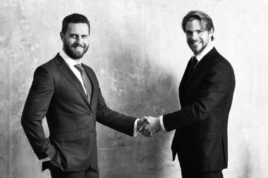 Ceketli mutlu adamlar el sıkışırken el ele tutuşuyorlar.