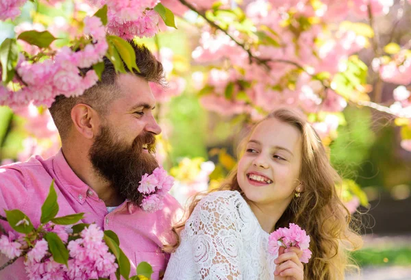 Koncepcja dzieciństwa. Dziewczyna z tata w pobliżu sakura kwiaty na dzień wiosny. Dziecko i człowiek z przetargu różowe kwiaty w brodę. Ojciec i córka na szczęśliwe twarze gry z kwiatami i tulenie tło sakura — Zdjęcie stockowe
