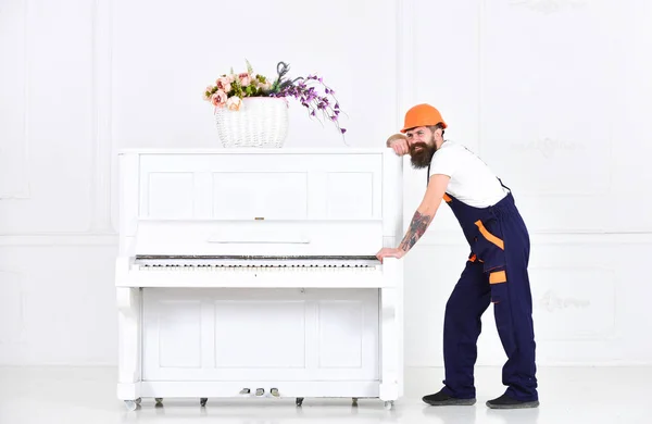 Strong worker having a break isolated on white background. Smiling guy with mustache trying to move white piano. Long day at work