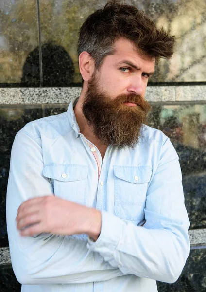 Masculinity concept. Guy looks suspicious. Hipster with tousled hair hold arms crossed on chest. Man with beard and mustache on thoughtful, pensive face, black marble background