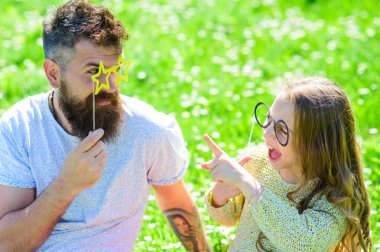 Baba ve kızı, grassplot, arka planı yeşil çimenlerin üzerinde oturur. Çocuk ve babası eyeglases photo booth özniteliği ile konuşurken poz. İletişim kavramı. Aile harcamak açık havada eğlence