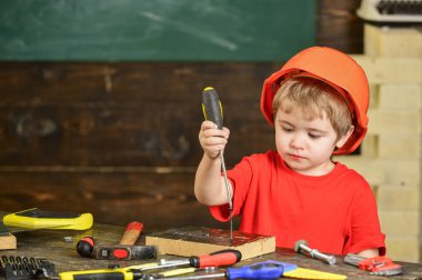 Tornavida ile çalışma meşgul bir çocuk. Turuncu kask vida ahşap blok içine bağlama içinde çocuk konsantre