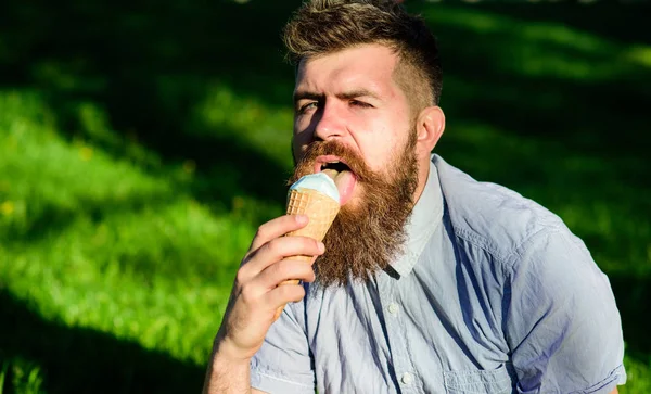 Skäggig man med glasstrut. Delikatess koncept. Man med långt skägg äter glass, samtidigt sitter på gräset. Mannen med skägg och mustasch på sexig ansikte slickar glass, gräs på bakgrund, oskärpa — Stockfoto