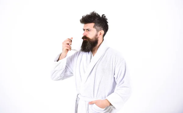 Hombre guapo en un albornoz sosteniendo una taza aislada sobre fondo blanco. Un tipo barbudo bebiendo café o té por la mañana. Serenidad matutina —  Fotos de Stock