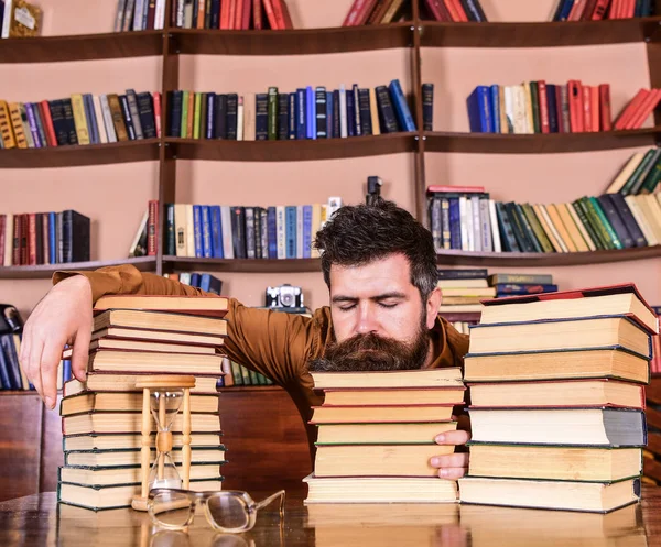 Homem no rosto dormindo estava entre pilhas de livros, adormecer enquanto estudava na biblioteca, estantes de livros no fundo. Conceito demasiado estudado. Professor ou estudante com barba adormecer em livros, desfocado — Fotografia de Stock