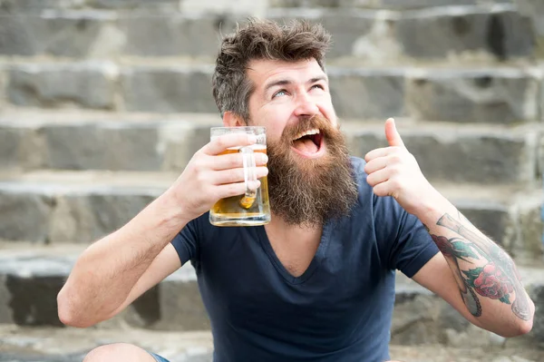 Feliz hombre barbudo tomando una copa después de un largo día en la oficina. Alegre hombre borracho sosteniendo taza de cerveza mientras muestra el gesto de pulgar hacia arriba, relajarse después del trabajo y el concepto de fin de semana — Foto de Stock