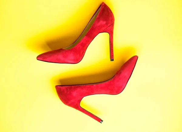 Feminine shoes concept. Footwear with thin high heels, stiletto shoes, top view. Shoes made out of red suede on yellow background. Pair of fashionable high heeled pump shoes