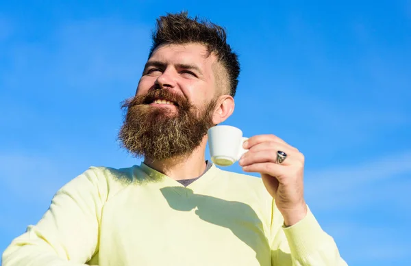 Homem com barba longa desfrutar de café. Homem com barba e bigode no rosto sorridente bebe café, fundo azul do céu, desfocado. Homem barbudo com caneca de café, bebe café. Conceito de provador de café — Fotografia de Stock