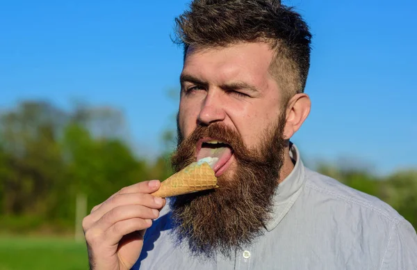 Sweet tooth concept. Bebaarde man met ijsje. Man met lange baard likt ijs. Man met baard en snor op strikte gezicht eet ijs, blauwe hemelachtergrond, intreepupil — Stockfoto