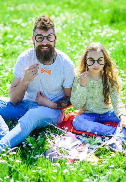 O pai e a filha sentam-se na relva no campo, fundo verde. Criança e pai posando com óculos atributos de cabine de fotos no prado. Família passar o lazer ao ar livre. Conceito inteligente e inteligente — Fotografia de Stock