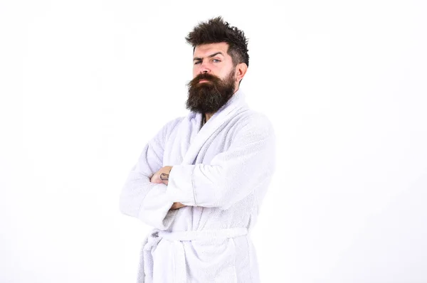 Hombre guapo en un albornoz aislado sobre fondo blanco. Un barbudo de pie con los brazos cruzados en el pecho. Macho en pijama frunciendo el ceño y levantando la ceja —  Fotos de Stock