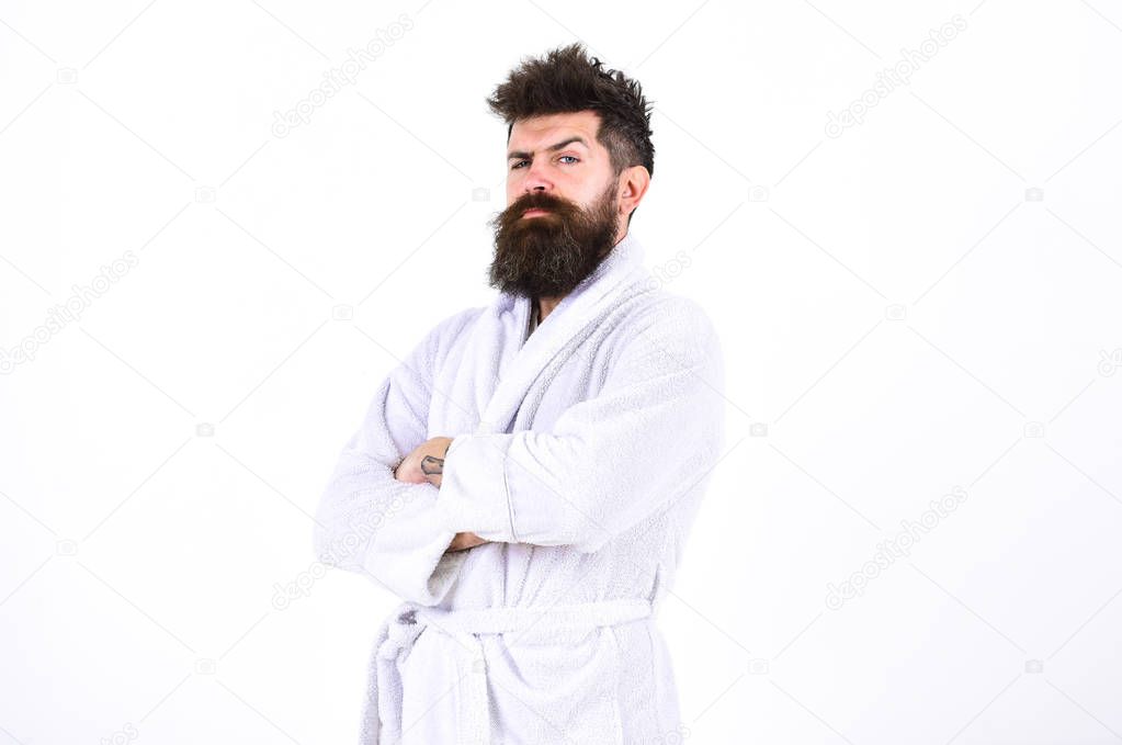 Handsome man in a bathrobe isolated on white background. Bearded guy standing with arms crossed at his chest. Macho in pajamas frowning and raising his eyebrow