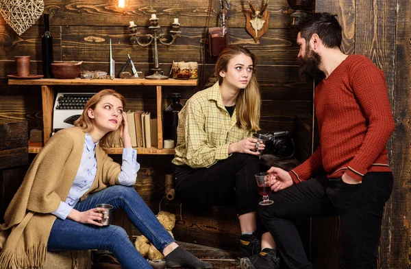 Friends, family spend pleasant evening, interior background. Sincere conversation concept. Girls and man on happy faces hold metallic mugs, talking. Family enjoy conversation in gamekeepers house