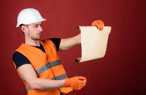 Architect concept. Man in helmet, hard hat holds building plan, controls works, red background. Engineer, architect, builder on strict face holds old blueprint in hands, supervises construction site — Stock Photo, Image