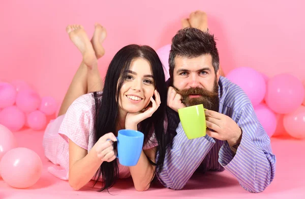 Pár reggel kávéval lazítson. A pár a szerelem kávét iszik az ágyban. Férfi és nő a mosolygó arcok feküdt, rózsaszín háttér. Hétvégén reggel koncepció. Férfi és nő a hazai ruházat, pizsama — Stock Fotó