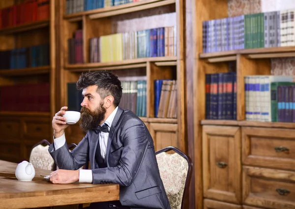 ビジネスマンはヴィンテージのインテリアに座って、本とお茶のカップを保持します。キャビネットの高級スーツを着た髭の男。穏やかな顔の熟女は読書を楽しんでいます.高級ライフスタイル、ヴィンテージファッション、お茶のコンセプト — ストック写真