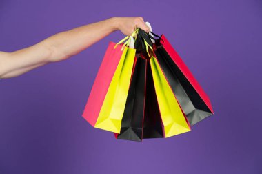 Menekşe arka plan üzerinde elinde poşetler. Farklı renklerde kağıt torbalar. Çanta veya paperbags. Alışveriş veya satış ve siyah Cuma kavramı. Tatil hazırlanması ve kutlama. Hediye ve hediye.