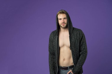 Sakallı adam menekşe arka planda kapüşon takıyor. Sıradan tişörtlü, seksi vücutlu bir maço. Kapüşonlu manken. Aktif yaşam tarzı ve sağlık aktiviteleri. Moda tarzı ve trend konsepti, alanı kopyala.