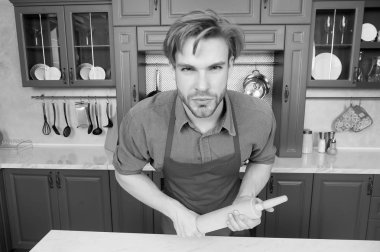 Kırmızı şef önlüklü maço, mutfaktaki masada merdane duruyor. Pişir, pişir, pişir, pişir. Ev yemeği konsepti