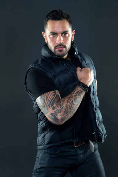 Man with tattoo on strong arm skin. Tattooed man in trendy clothes. Fashion macho with confidence and charisma. Tattoo model with beard on unshaven face. Fashion or style and trend.