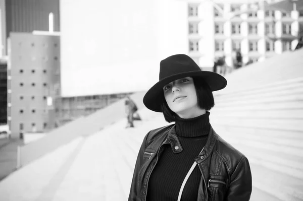 Girl in black hat and jacket pose on stairs. Woman with natural makeup face and brunette hair outdoor. Ambition, challenge, success concept. Fashion and accessory. Look, beauty, style. Parisian woman
