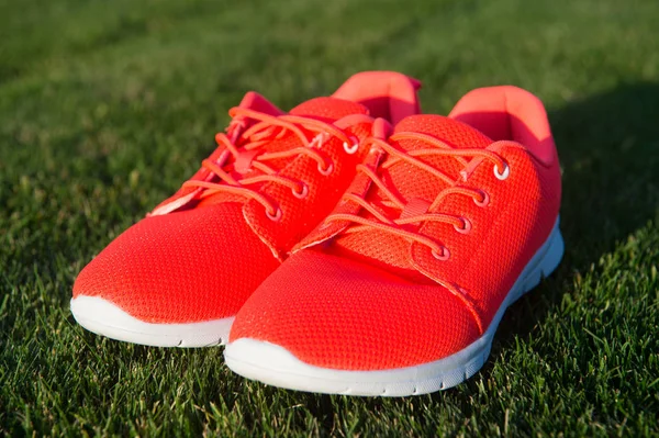 Run the life! Sneakers on green grass. Pair of sneakers on sunny outdoor. Sport shoes of orange fabric material on white sole. Fashion style and trend. Sport and active lifestyle.