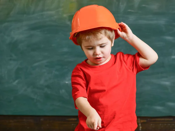 Jungen spielen als Bauarbeiter oder Architekt. Junge mit orangefarbener Mütze oder Helm, Kreidetafel im Hintergrund. Kind, das von einer Karriere in der Architektur oder im Bauwesen träumt. Kindheitskonzept — Stockfoto