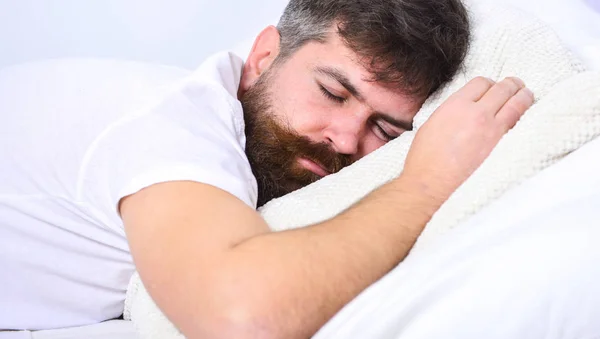 Yatakta, arka plan üzerinde beyaz duvar döşeme tişörtlü adam. Maço sakal ve bıyık uyku, rahatlatıcı, nap, sahip rest. NAP ve siesta kavramı. Adam sakin yüz beyaz çarşaf ve yastık uyku — Stok fotoğraf
