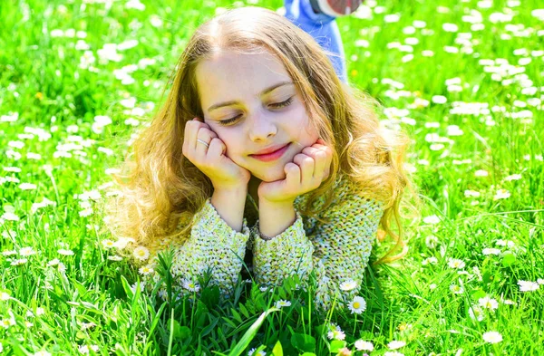Dívka ležící na trávě na pastvinách, zelené pozadí. Dívka na zasněné tváři tráví volný čas venku. Heyday koncept. Dítě vychutnat jarní slunečné počasí, zatímco leží na louce — Stock fotografie