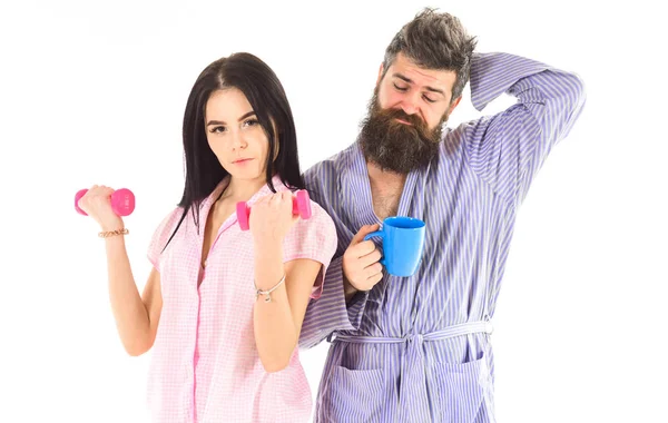 Chica con mancuerna, hombre con taza de café, aislado sobre fondo blanco. Pareja, familia con caras somnolientas en la rutina matutina. Concepto de energía matutina. Pareja enamorada en pijama, albornoz espalda con espalda —  Fotos de Stock