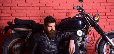 Yenilikçi, vahşi Motorcu deri ceketli dalgın yüzündeki motosiklet yakın yerde oturamaz. Vahşi motorcu kavramı. Sakallı, motorcu motorlu bisiklet garaj, tuğla duvar arka plan yakınındaki deri ceketli adam.