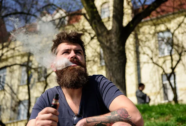 Concepto de aspiración y hábitos. Hombre con barba y bigote fumando, fondo urbano. Hipster con el pelo acariciado y gris en la cara de ensueño relajado con humo blanco que vuela por la boca —  Fotos de Stock