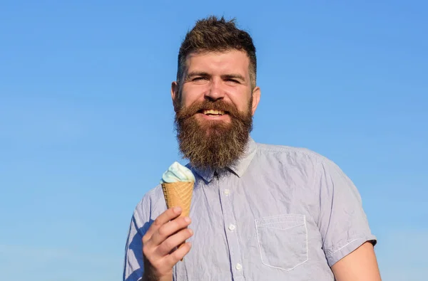 Homem com barba longa gosta de sorvete. Conceito dos dentes doces. Homem com barba e bigode no rosto sorridente come sorvete, fundo azul do céu, desfocado. Homem barbudo com cone de sorvete — Fotografia de Stock