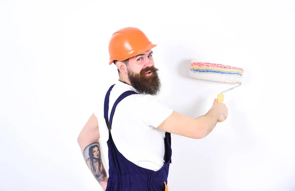 Koncepce domácí vymalování. Zase usměvavá tvůrce malby zdi s válečkem. Izolované muž v oranžovou helmu a celkově na bílém pozadí — Stock fotografie