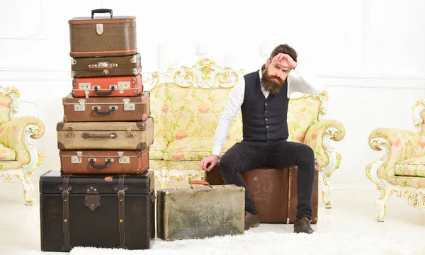 Macho elegant mit strenger Miene sitzt müde neben einem Stapel Vintage-Koffer. Mann, Butler mit Bart und Schnurrbart liefert Gepäck, luxuriöser weißer Innenraum. Gepäck- und Umzugskonzept — Stockfoto