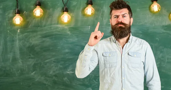 Lösning koncept. Skäggiga hipster i skjorta, svarta tavlan på bakgrund. Mannen med skägg och mustasch på allvarliga ansikte stå framme av svarta tavlan. Killen har idén eller varning visar pekfinger gest — Stockfoto